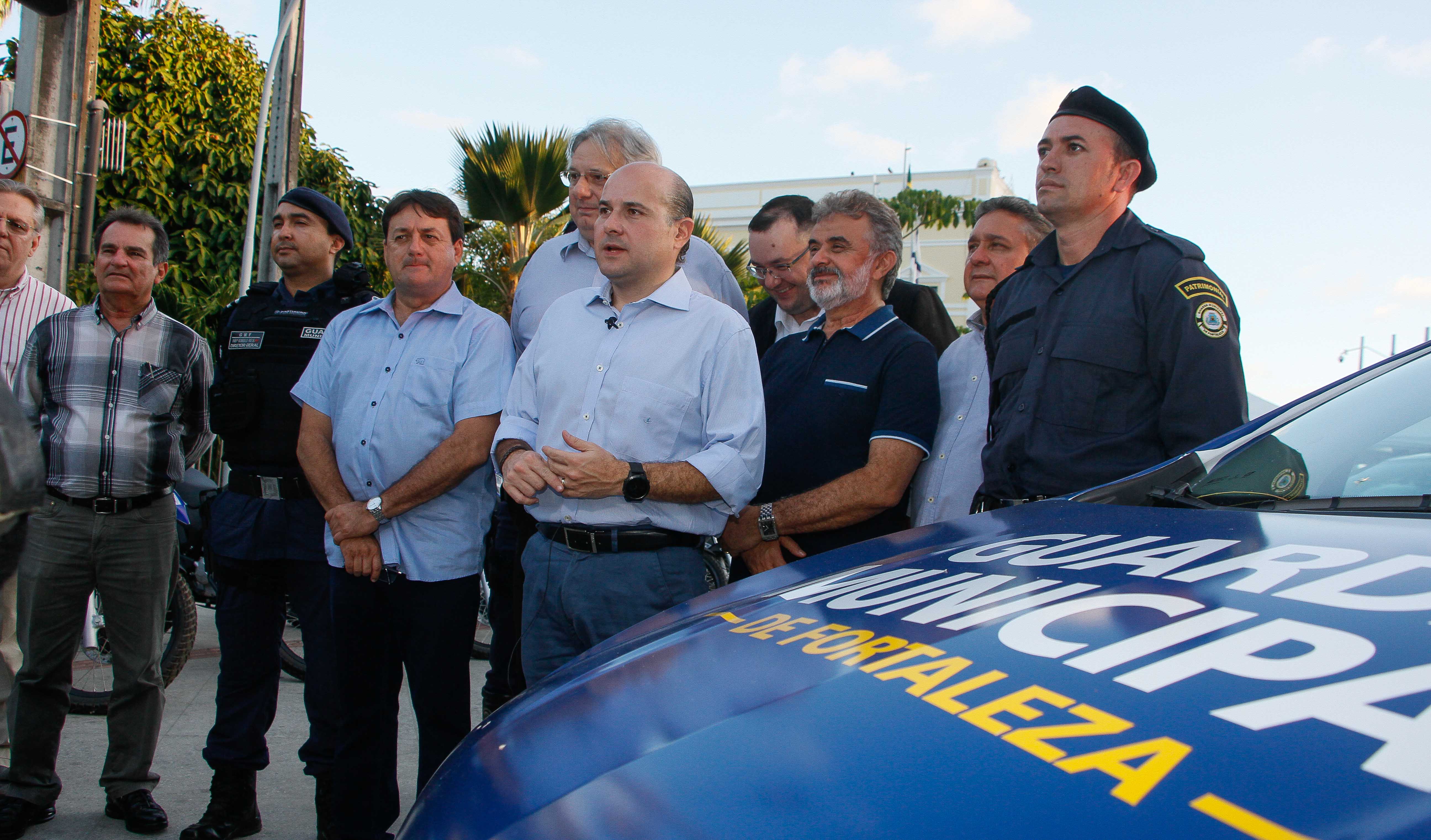 prefeito e outros senhores em pé ao lado de viatura